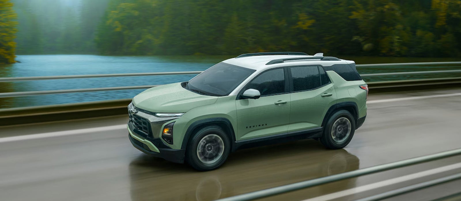 A light green 2026 Chevy Equinox SUV driving on a bridge over a river in the rain