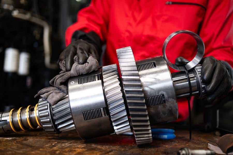 A mechanic in red coveralls holding a vehicle’s transmission